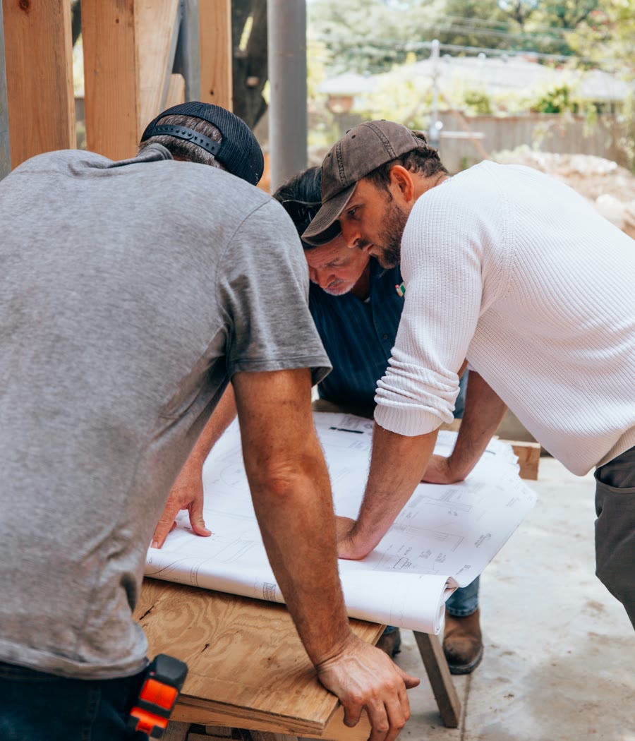 Three builders going over the plans on a sawhorse at a jobsite